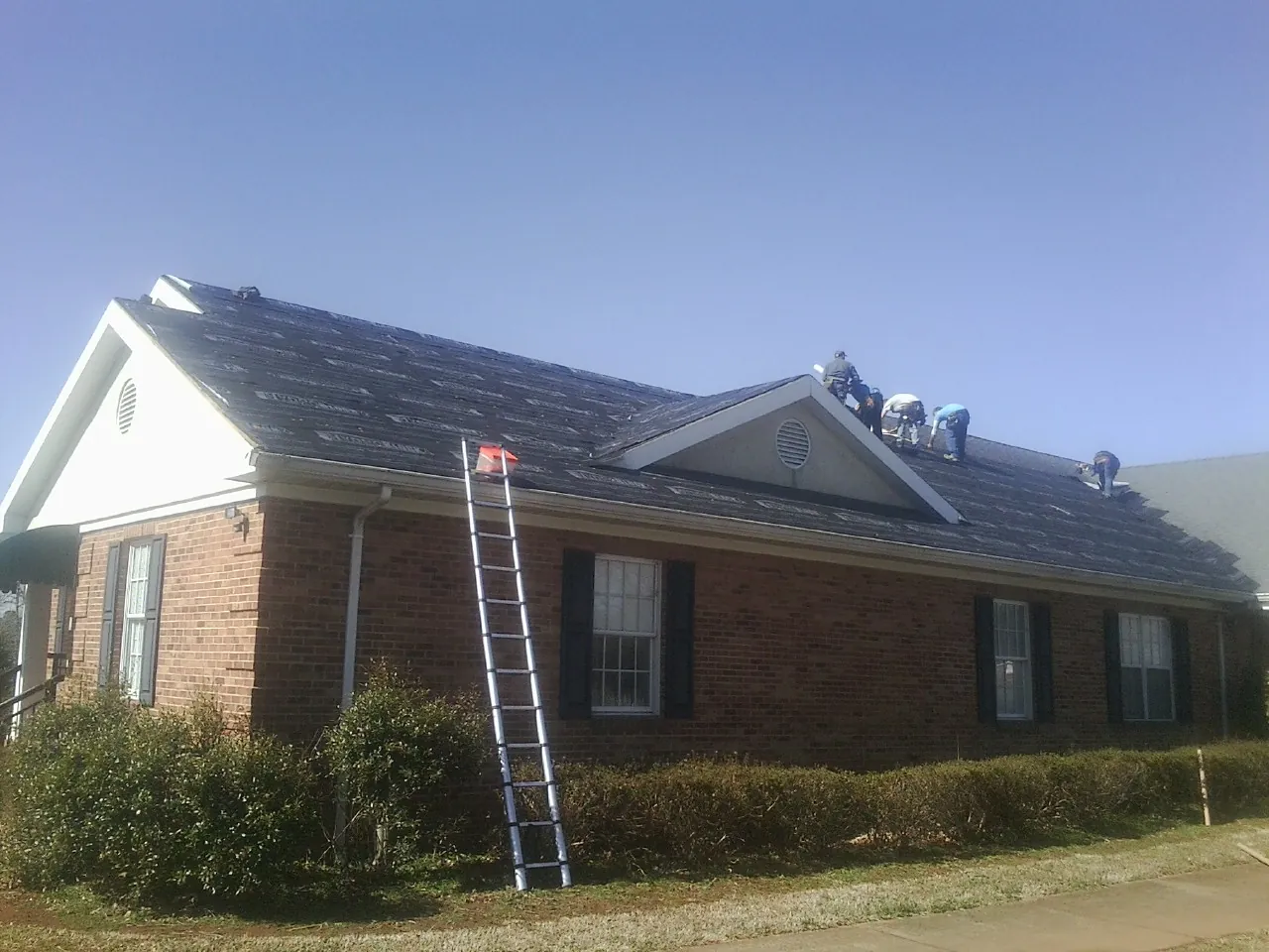 Crew tearing shingles off a brick ranch roof with a ladder set — Emergency Roof Repair work by our crew in Beverly Shores