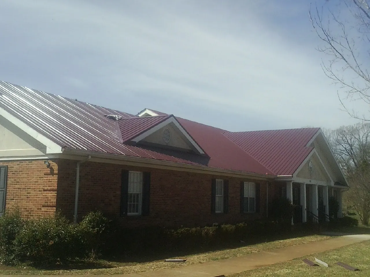 Red metal roof with gabled entries on a long brick building, from a Hail Damage Roof Repair job in Beverly Shores