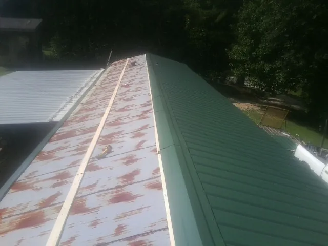 Old rusted panels beside newly installed green metal roofing — Wind Damage Roof Repair by Roofing Brothers in Beverly Shores