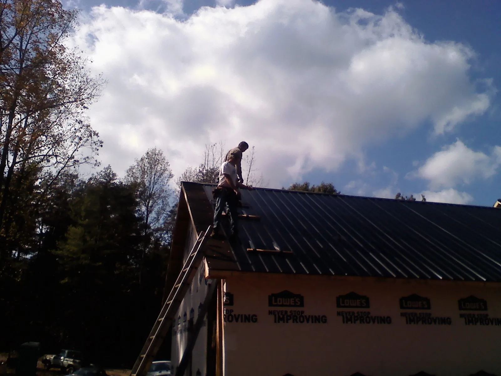 Roofer fastening dark metal panels high against a cloudy sky, from a Roof Inspection job in Beverly Shores