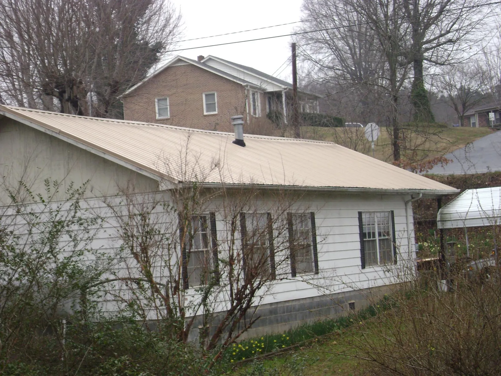 Tan metal roof on a white sided house set into a hillside — Commercial Roofing by Roofing Brothers in Beverly Shores